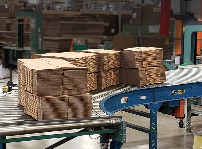 stacked flat boxes going down a manufacturing conveyor belt